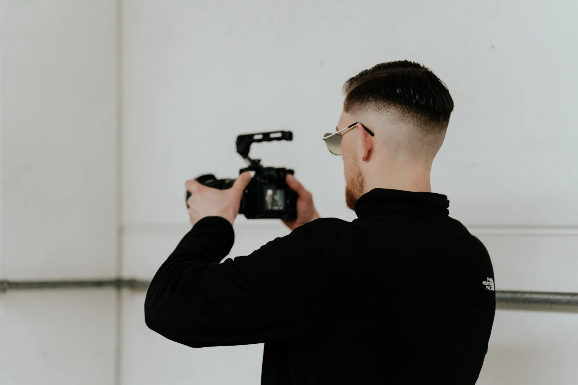 David Schulz filmt mit der Kamera an der Schulter, im Profil vor einer hellen Hallenwand.