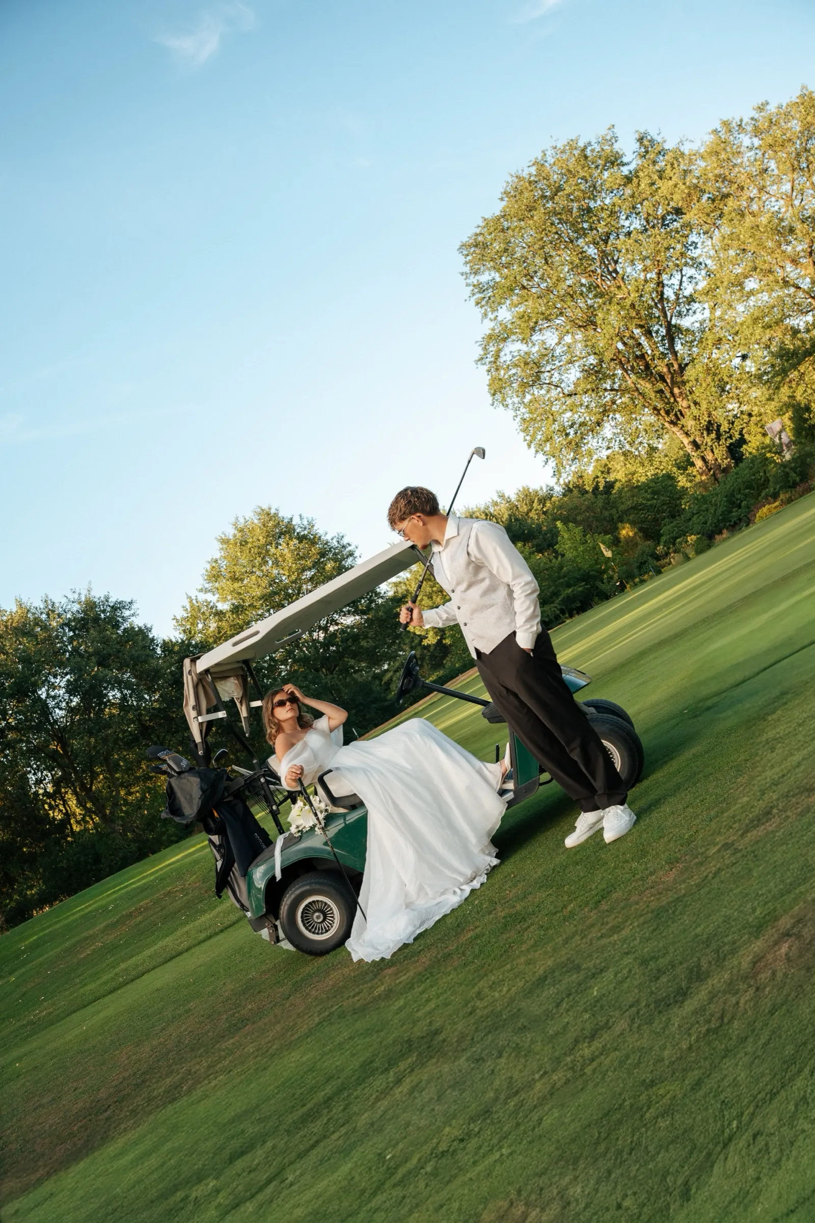 Weite Aufnahme des Golfplatzes: das Paar steht am Golfwagen unter offenem Himmel.